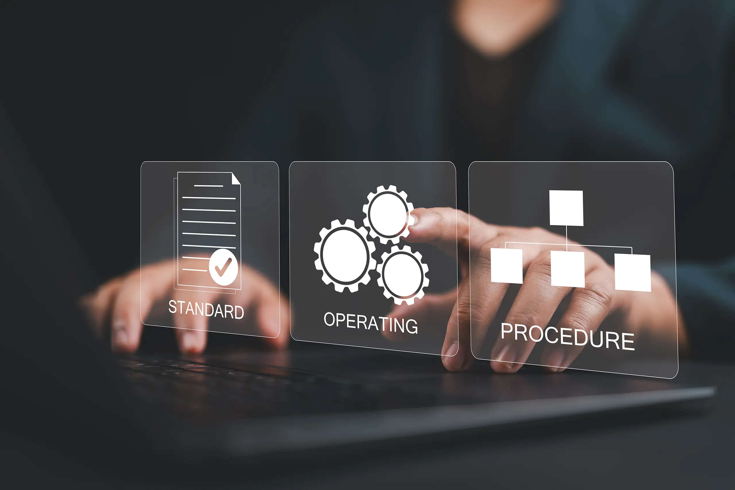Person on a latop top pointing to an overlaid graphic representing 'Operating' with cog wheel icons surrounded by other graphics representing 'Standard' and 'Procedure'