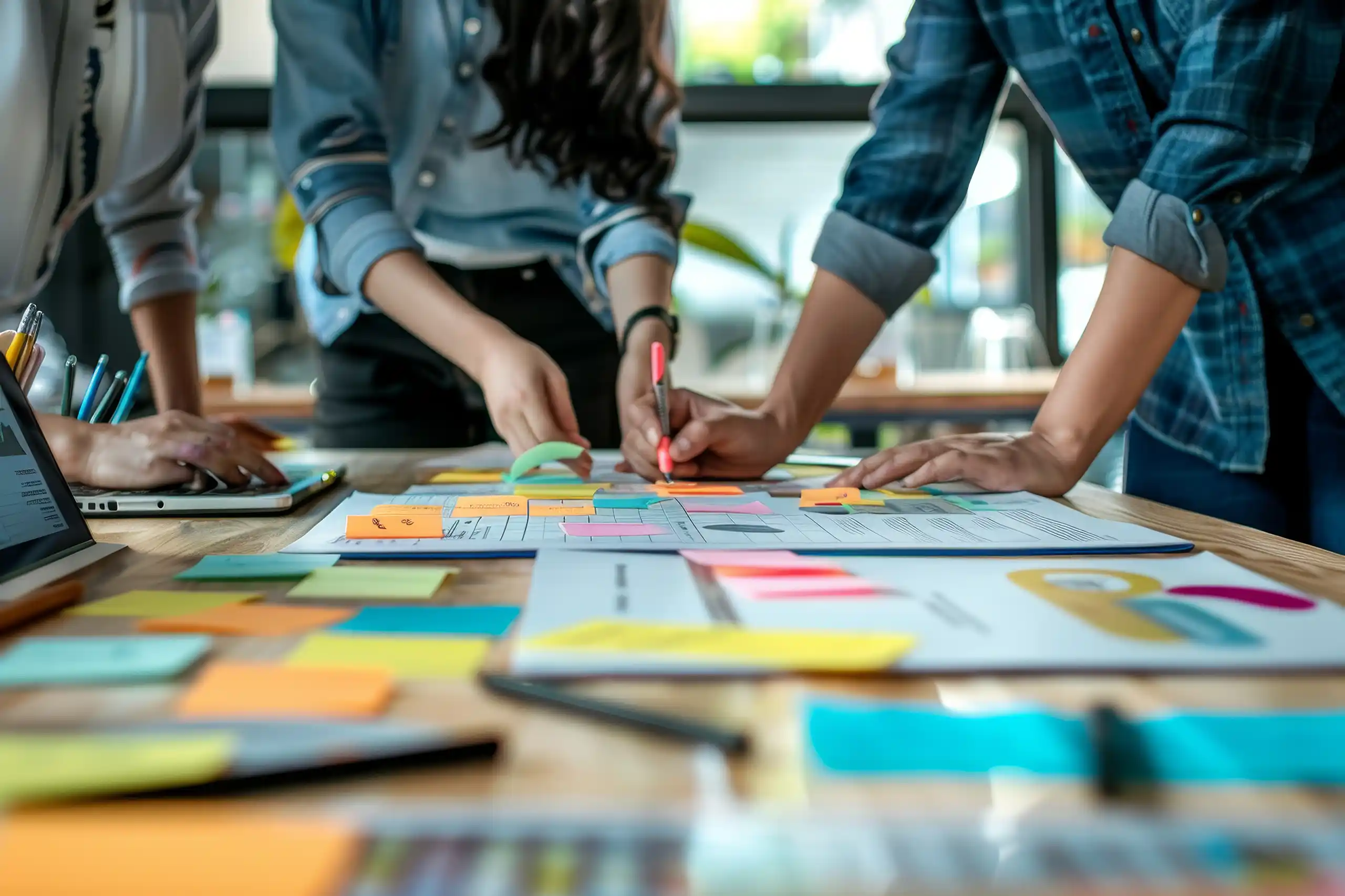 Three people stood around an office desk writing on post-it notes and analysing their work together
