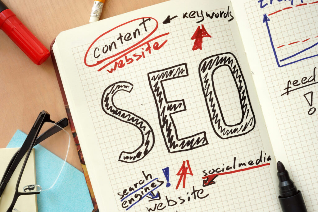 Notebook with the word “SEO” written in bold on a grid page, surrounded by related handwritten terms like content, keywords, website, and social media.