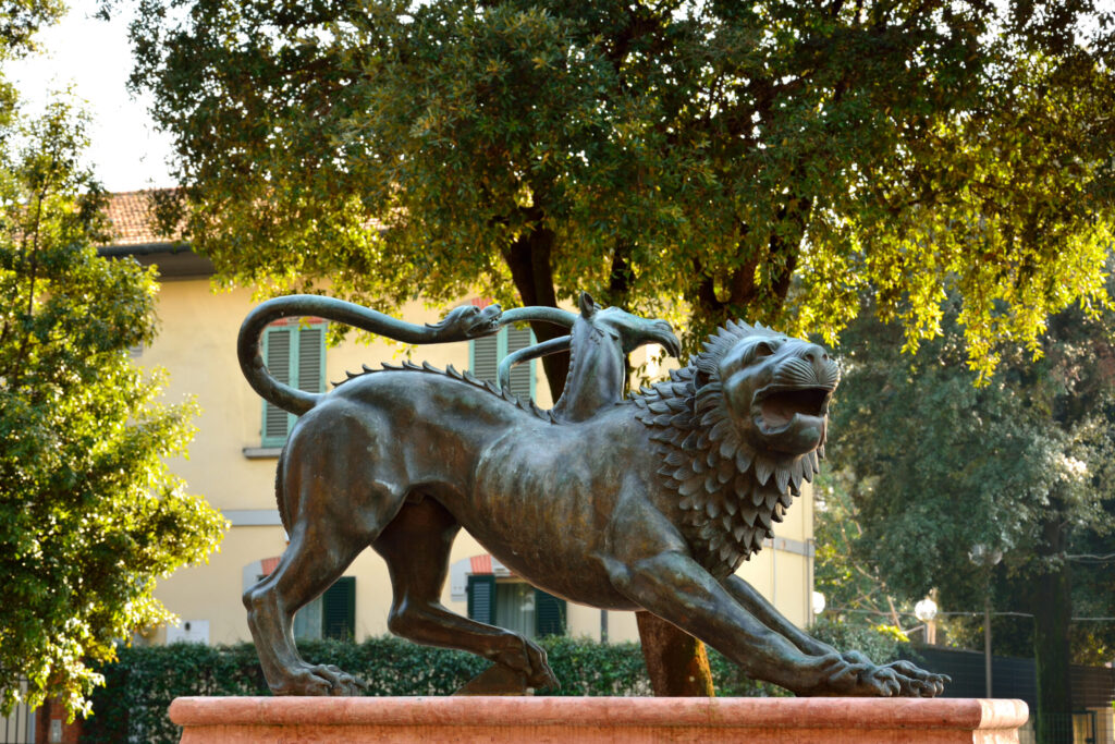 Bronze statue of the Chimera of Arezzo, a mythical creature with the body of a lion, a goat’s head on its back, and a serpent for a tail, displayed outdoors.