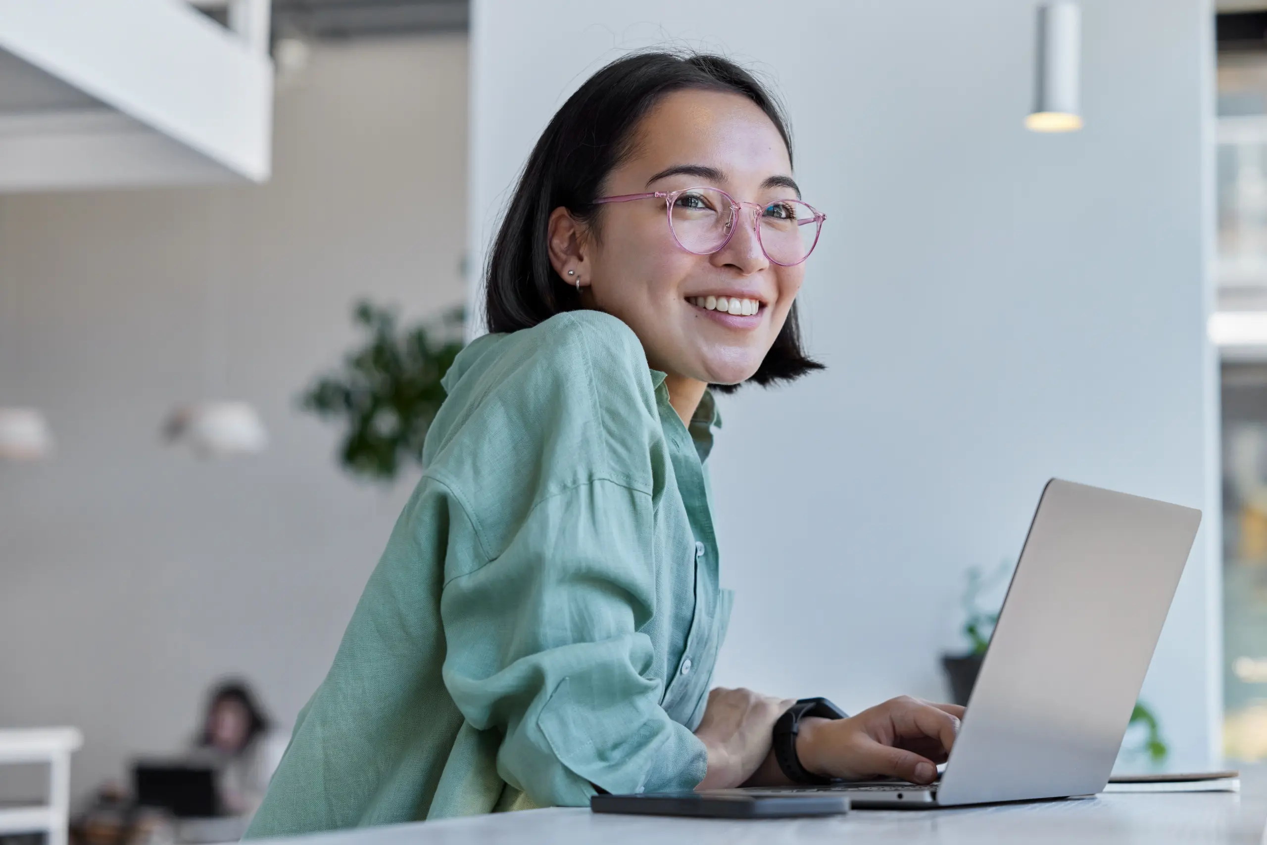 Young woman sitting on a desk with a laptop and smiling and looking over to her right