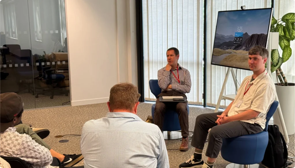 Two men presenting with a large screen, one demonstrating mobile accessibility as a blind user