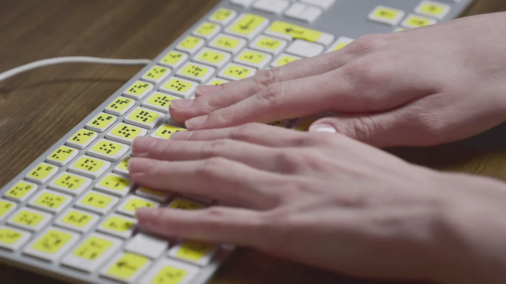 Closeup of hands typing on a braille keyboard with yellow keys